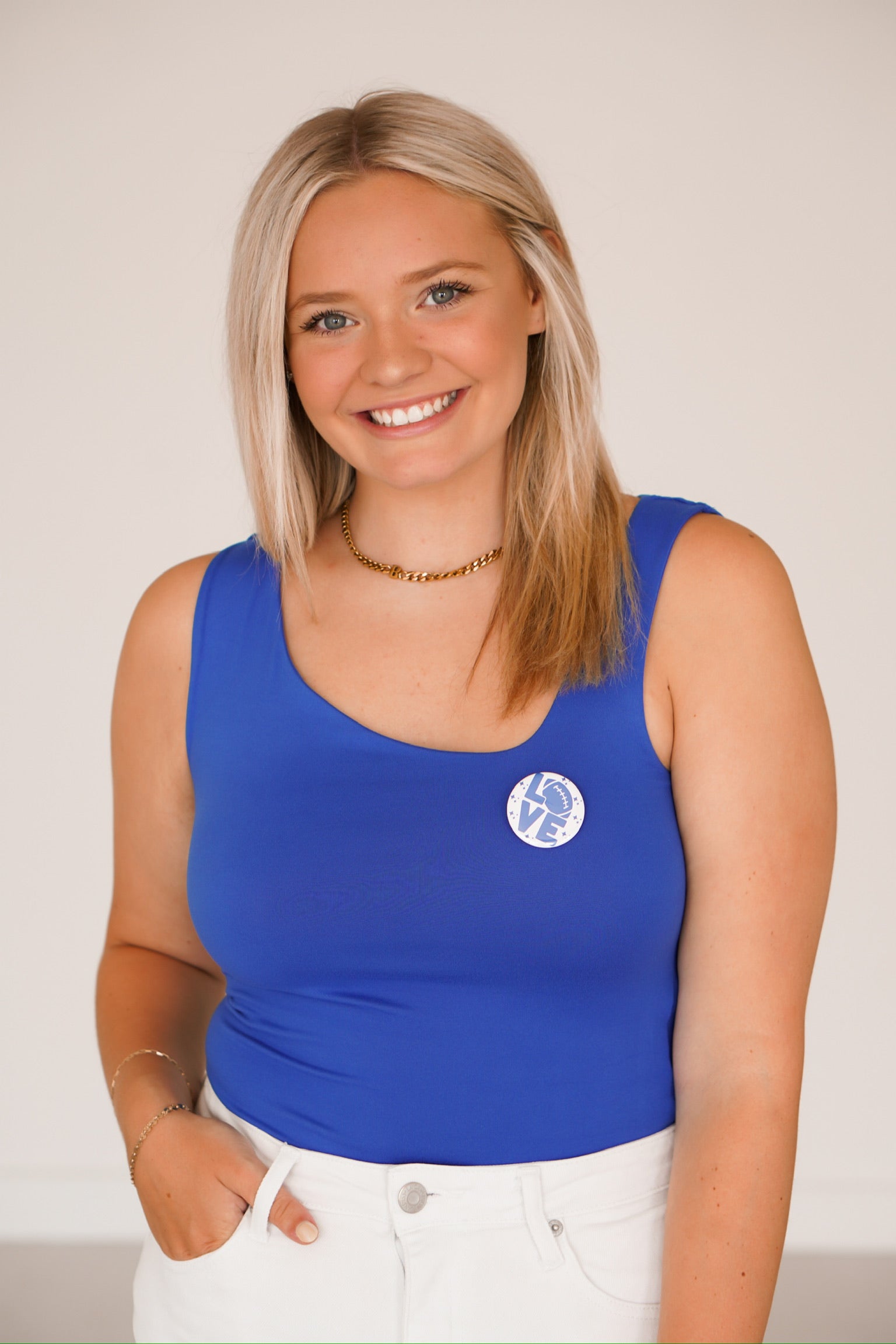 Blonde headed girl standing against a white wall wearing a royal blue top