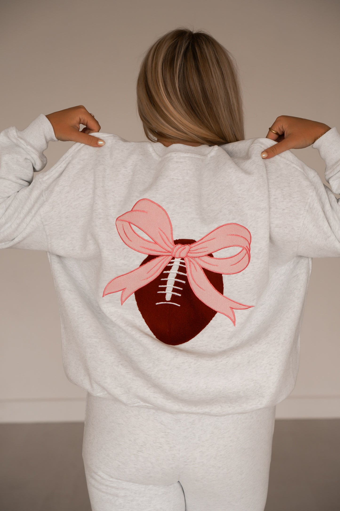 Showing an up close of the back of the grey sweatshirt that has a big football and pink bow on it