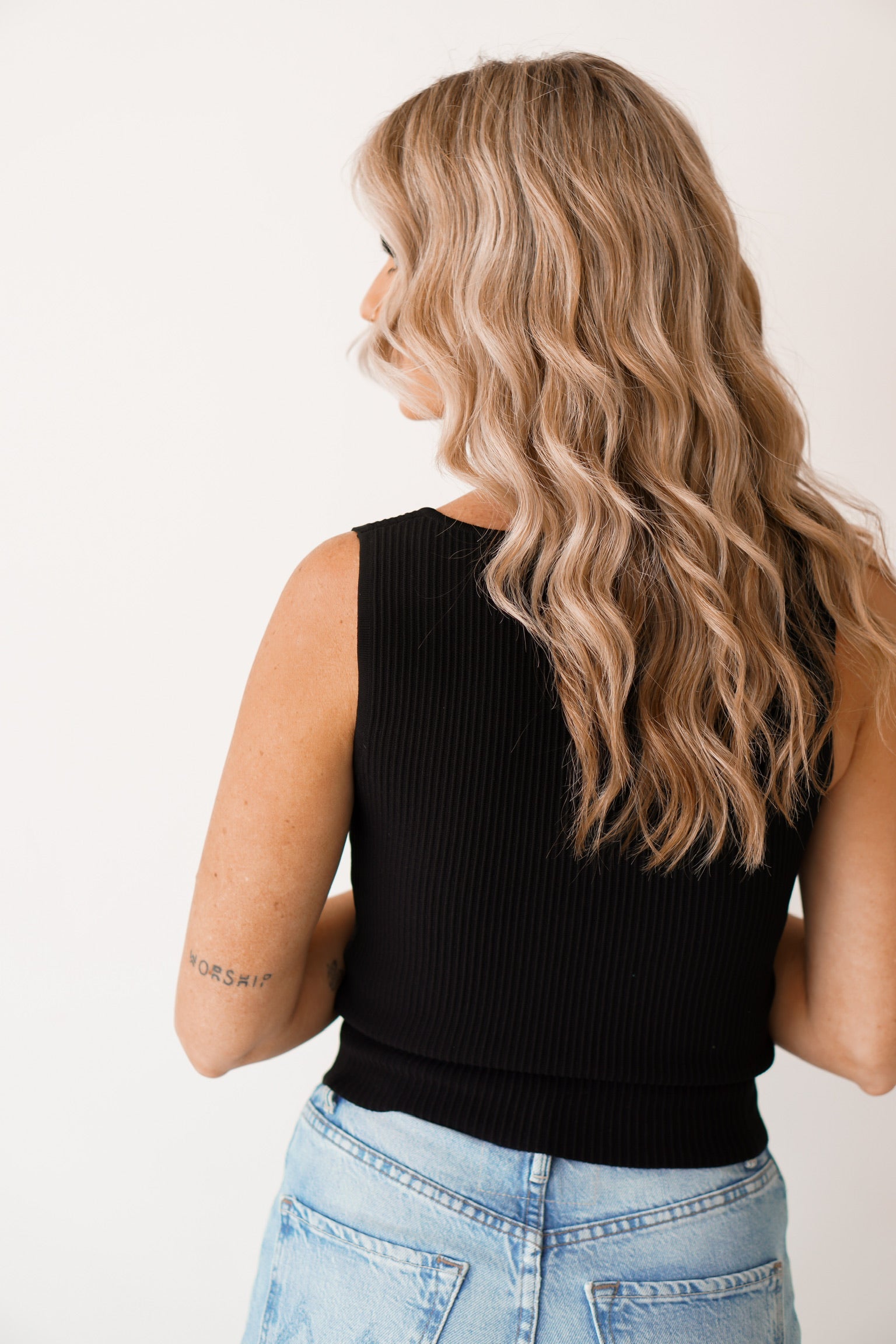 girl standing against a white wall, turned around backwards showing off the back of the tank 