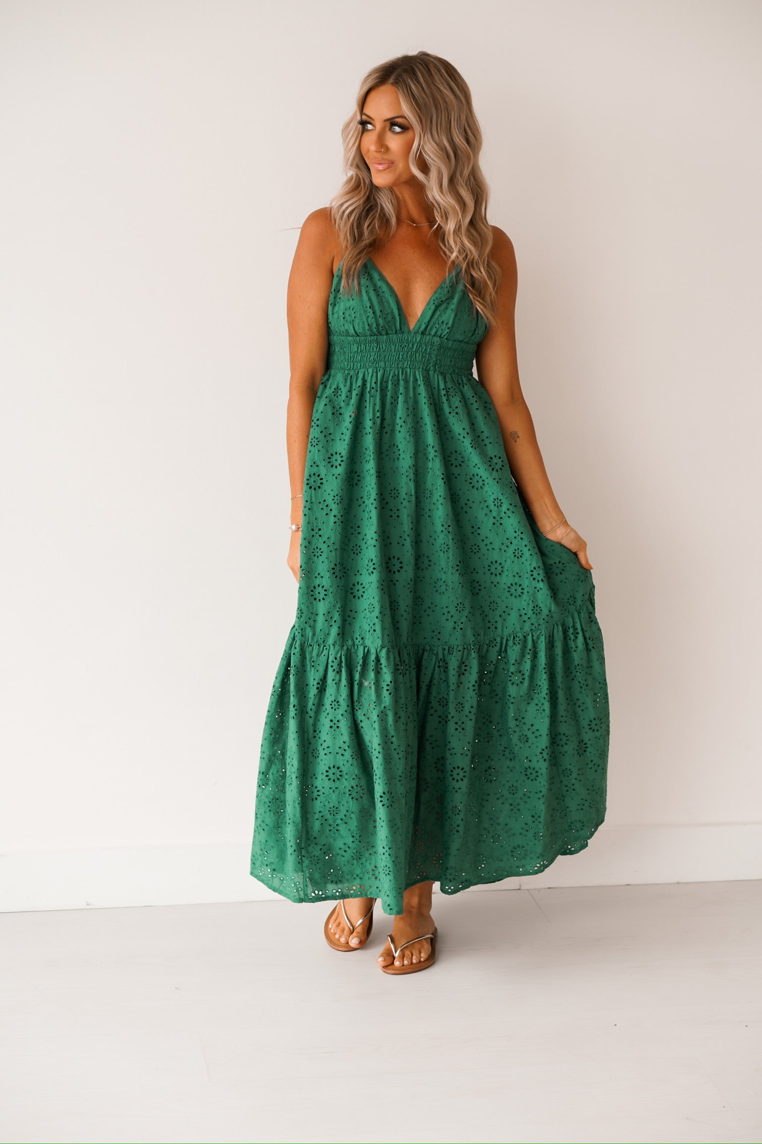 blonde  headed girl standing against a white wall wearing a green maxi dress and sandals