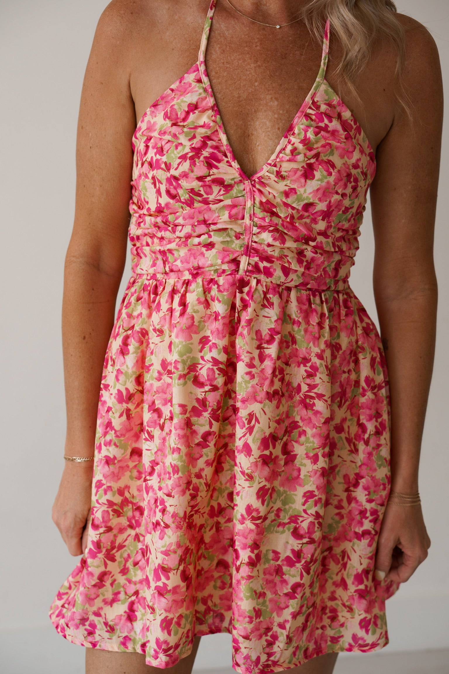 blonde headed girl standing against a white wall, wearing a short floral halterdress. 