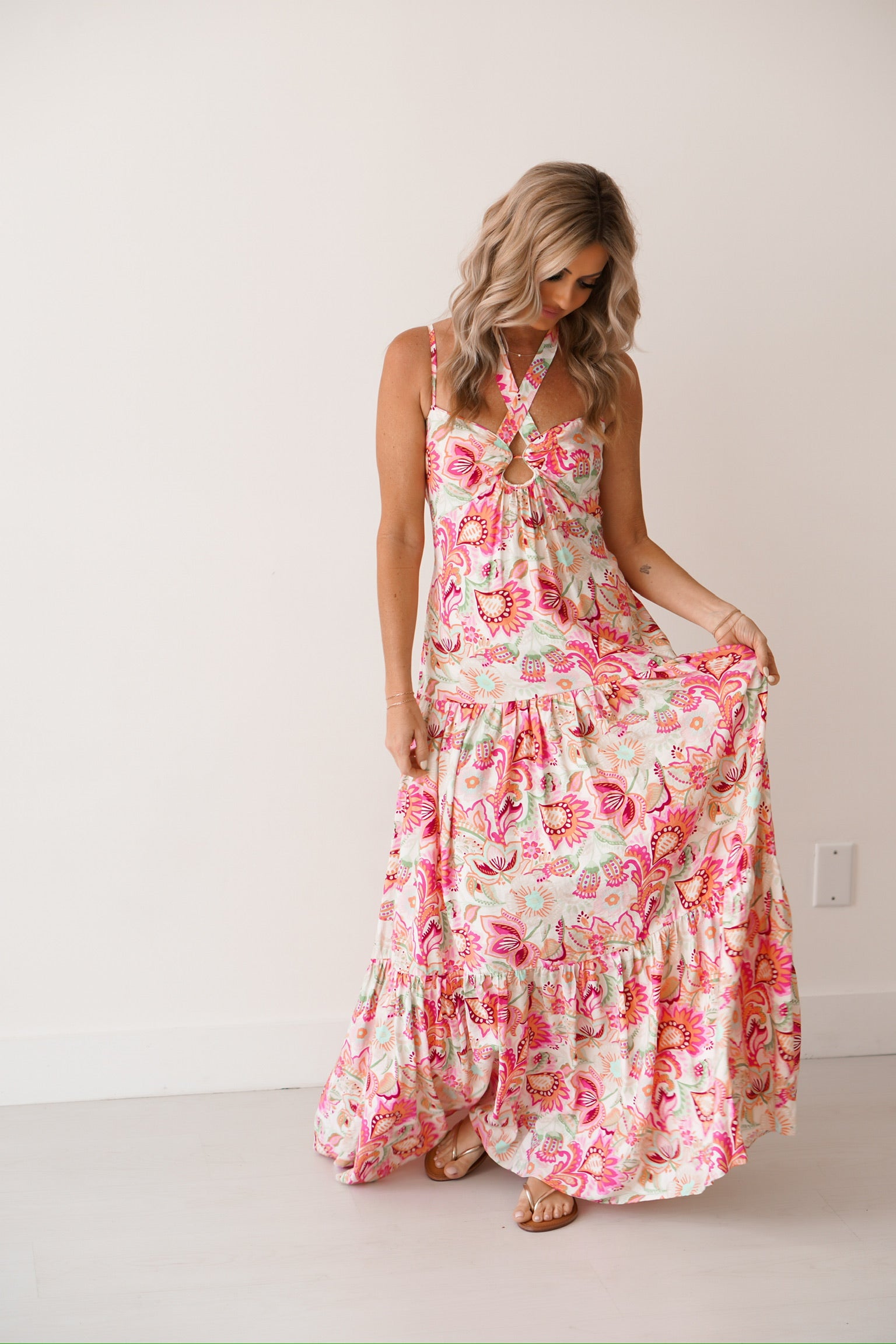 Blonde Girl standing against a white wall with a floral halter dress on. 