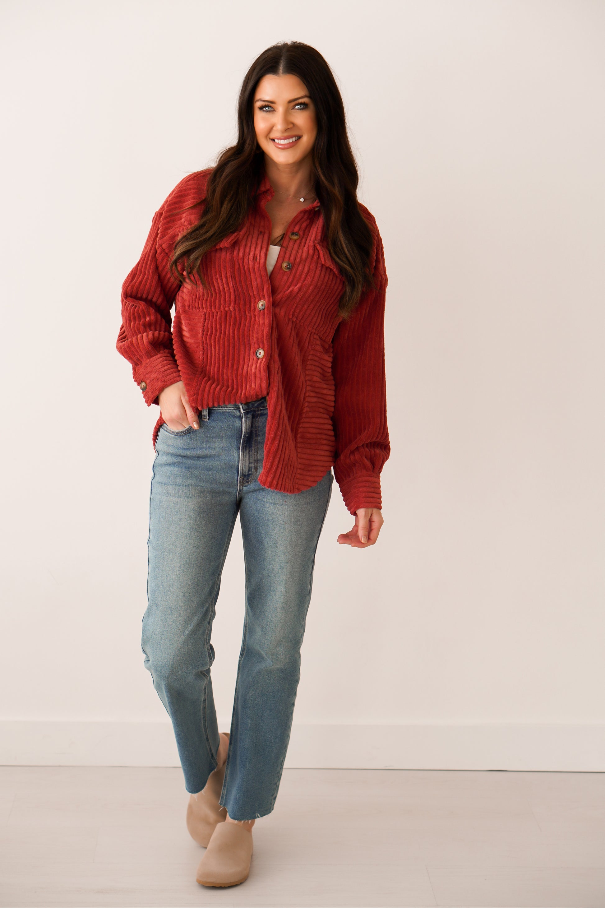 Brunette girl in a rust color shacket with brown buttons with her hand in her pocket. She is wearing jeans. 