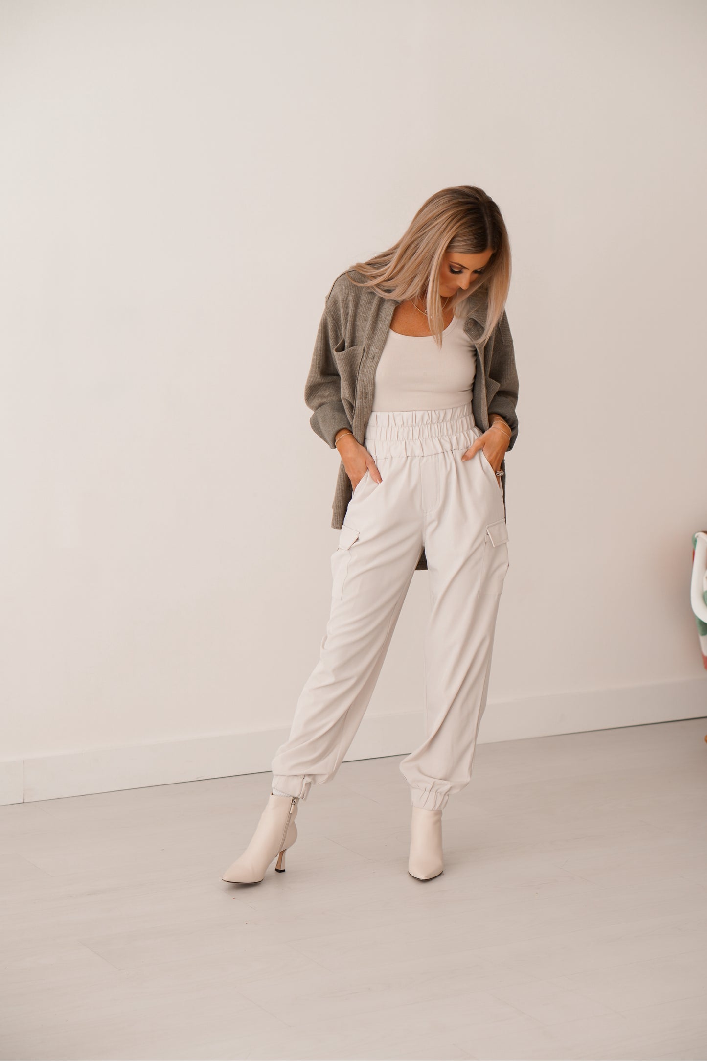 Blonde girl with cream tank, cream joggers and olive green shacket with her hands in her pockets. 