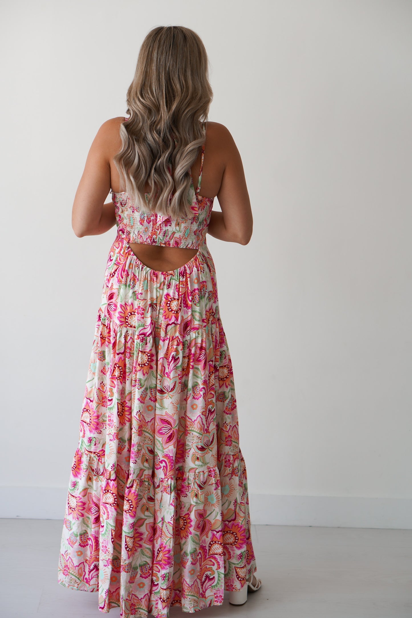 Blonde Girl standing against a white wall with a floral halter dress on. 