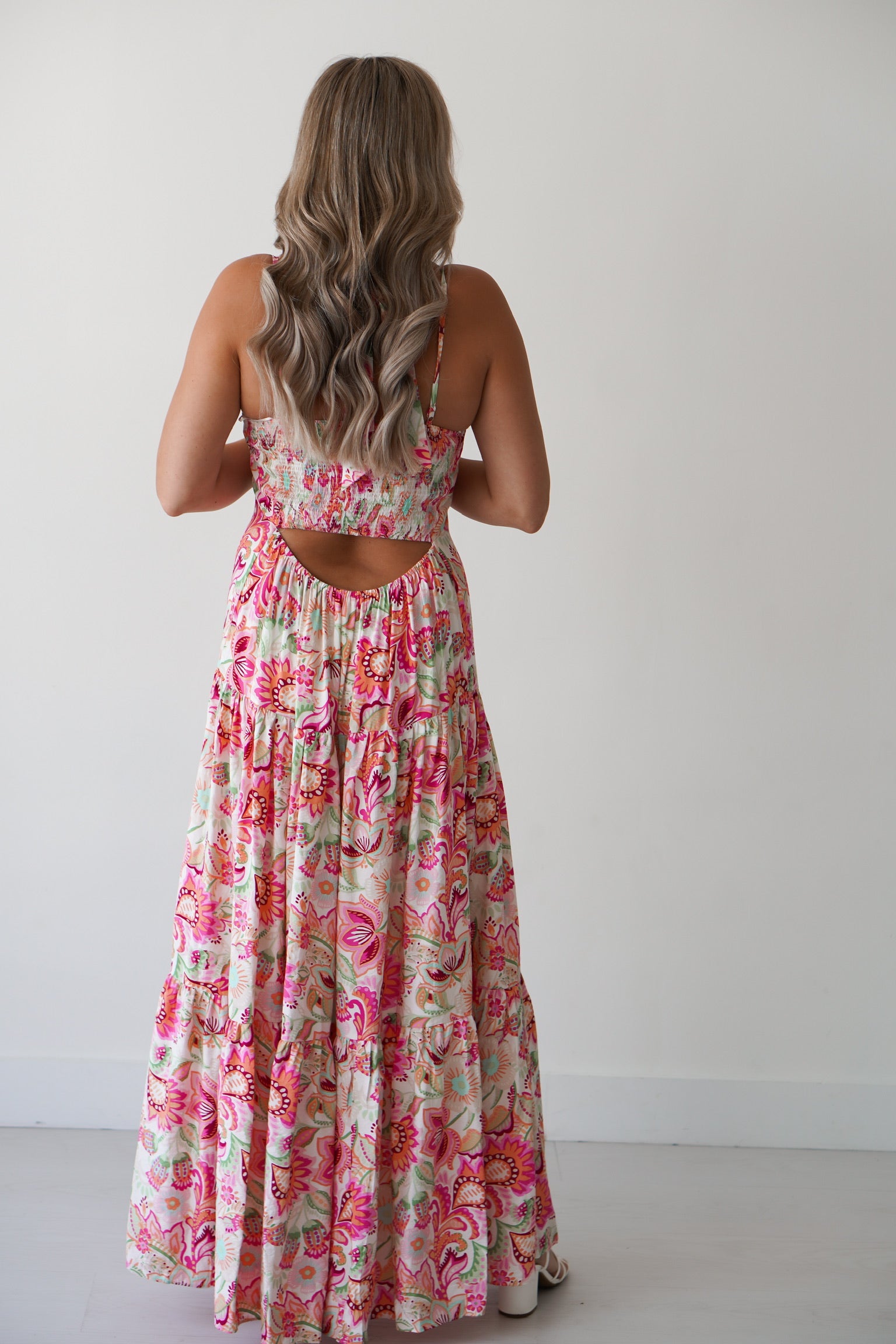 Blonde Girl standing against a white wall with a floral halter dress on. 