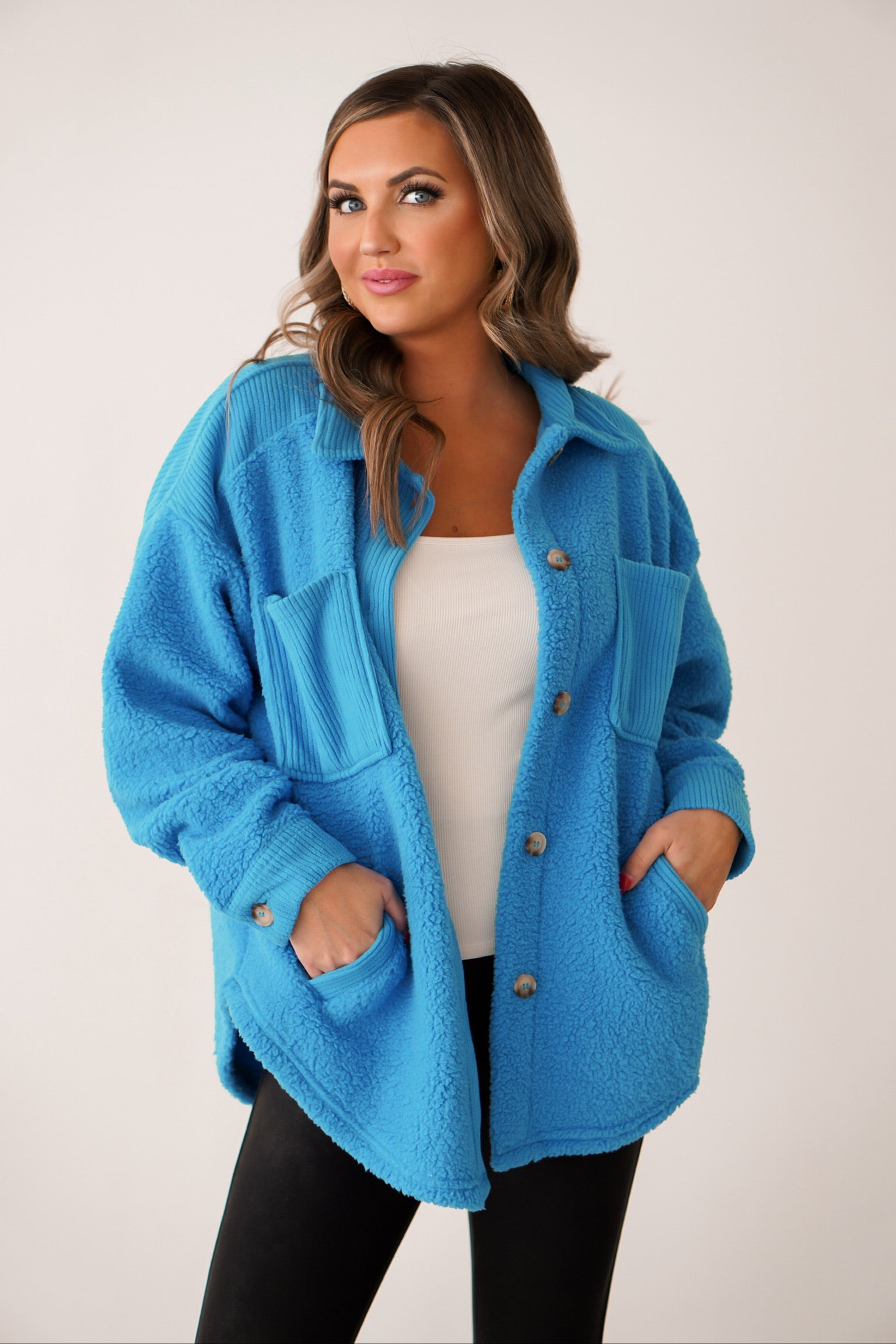 girl wearing a bright blue sherpa shacket with ribbed detail on shoulders with a white tank under and black leggings